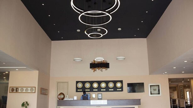 A hotel reception area with a modern chandelier, a reception desk, and framed clocks on the wall. - Ah Hotel and Conferences (Accra)