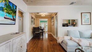 A spacious living area with a wooden floor, a sofa, a dining table with chairs, and a TV mounted on the wall. - Key West Cottage (West Palm Beach)