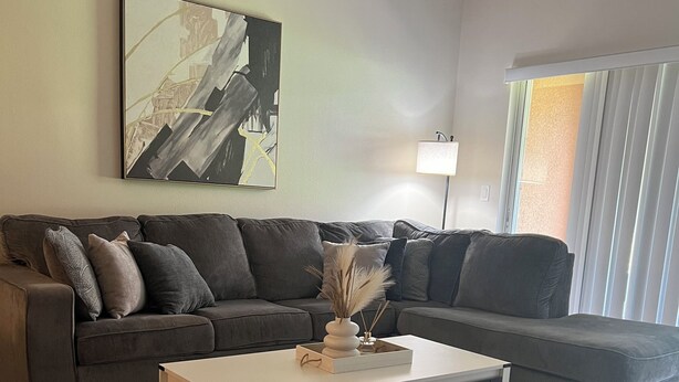 A living room with a grey sofa, a white coffee table with a decorative vase, and a large abstract painting on the wall. - Charming 2-bedroom townhome with WiFi, AC in brilliant Davenport (Davenport)