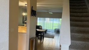 A spacious living area with a dining table, a trash can, and a staircase.