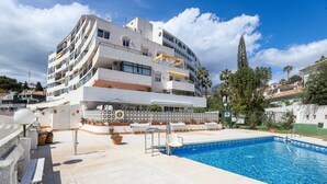 A modern building with a swimming pool, balconies, and a terrace with sun loungers.