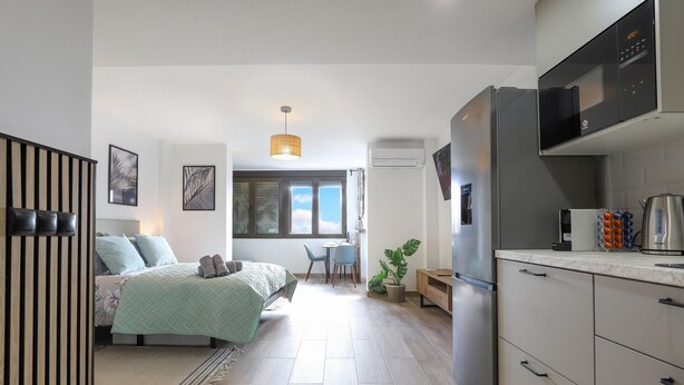 A modern bedroom with a bed, bedside tables, and a window. The room has a wooden floor and a ceiling light.