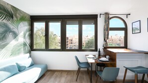 A modern living room with a sofa, dining table, chairs, and a large window with a view of buildings.