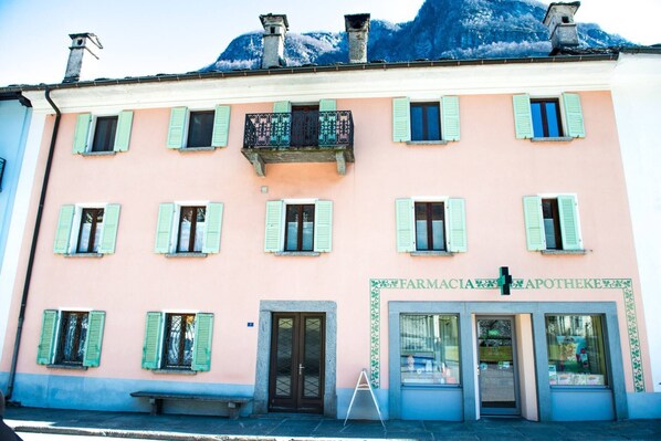 En lyserød bygning med grønne skodder og et skilt, der siger "FARMACIA APOTHEKE".
