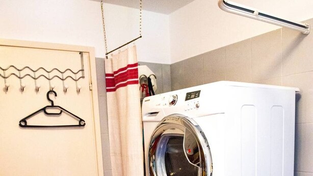 A laundry area with a stacked washer and dryer, a door with a hanger, and a curtain. - Charming Apartment in "cevio" in Vallemaggia (Cevio)