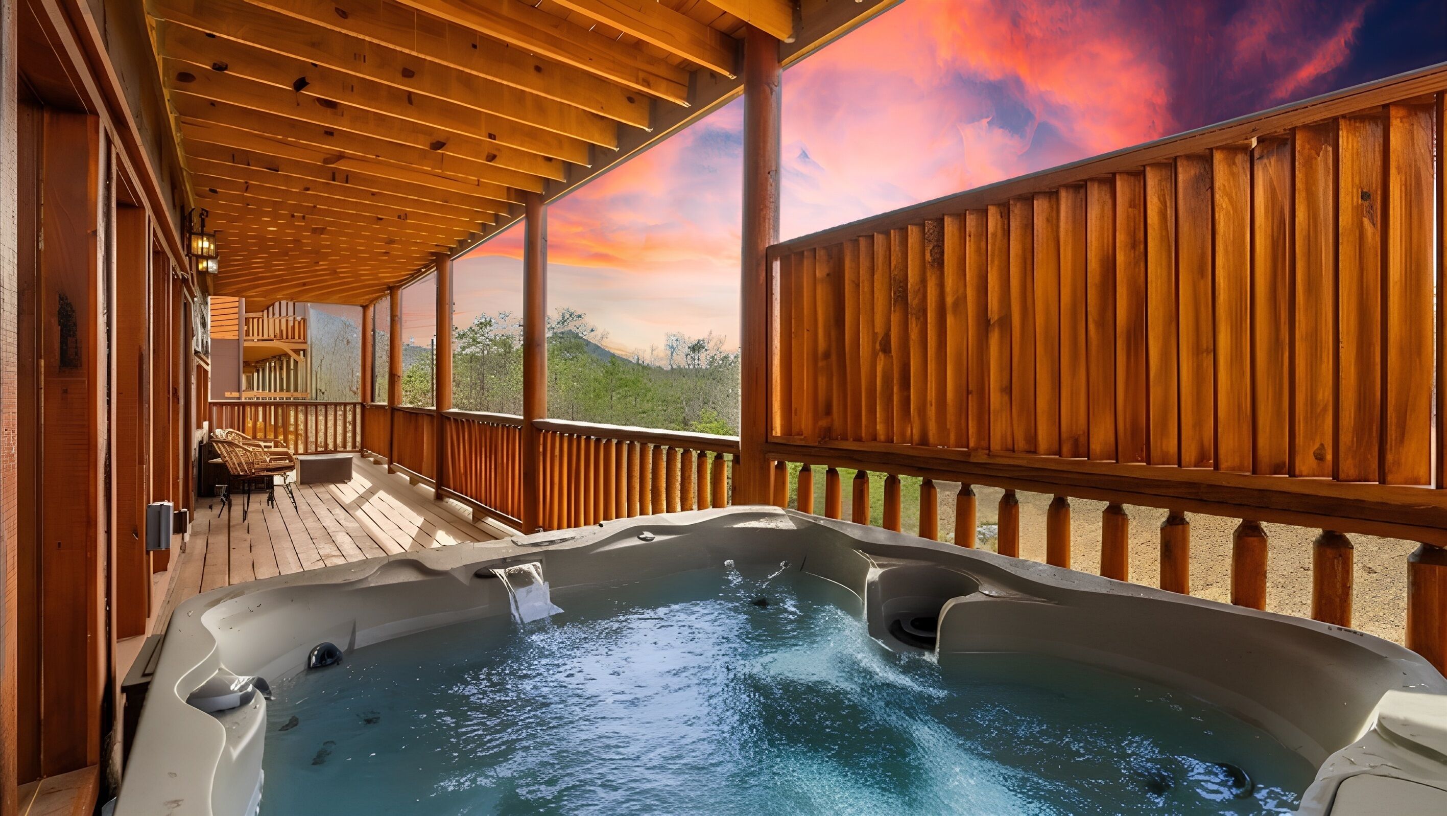 A hot tub on a wooden deck with a view of a sunset and greenery.