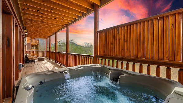 A hot tub on a wooden deck with a view of a sunset and greenery. - Luxe Family Cabin Pool Theater Hot Tub Game Room (Sevierville)