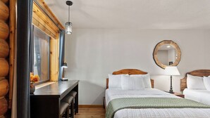 Ein Zimmer mit einem Holztisch, zwei Betten mit weißer Bettwäsche, einem runden Spiegel und einer hängenden Deckenleuchte.