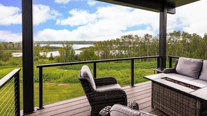 A covered outdoor deck with wicker furniture and a view of a lake and forest.