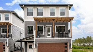 A two-story residential building with a garage, a covered balcony, and a well-maintained lawn.
