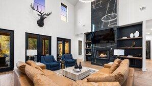 A spacious living room with leather sofas, a fireplace, and a mounted deer head.