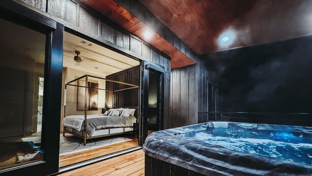 A modern bedroom with a four-poster bed, a wooden floor, and a hot tub.