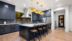 A modern kitchen with dark cabinetry, a central island with bar stools, stainless steel appliances, and pendant lighting.