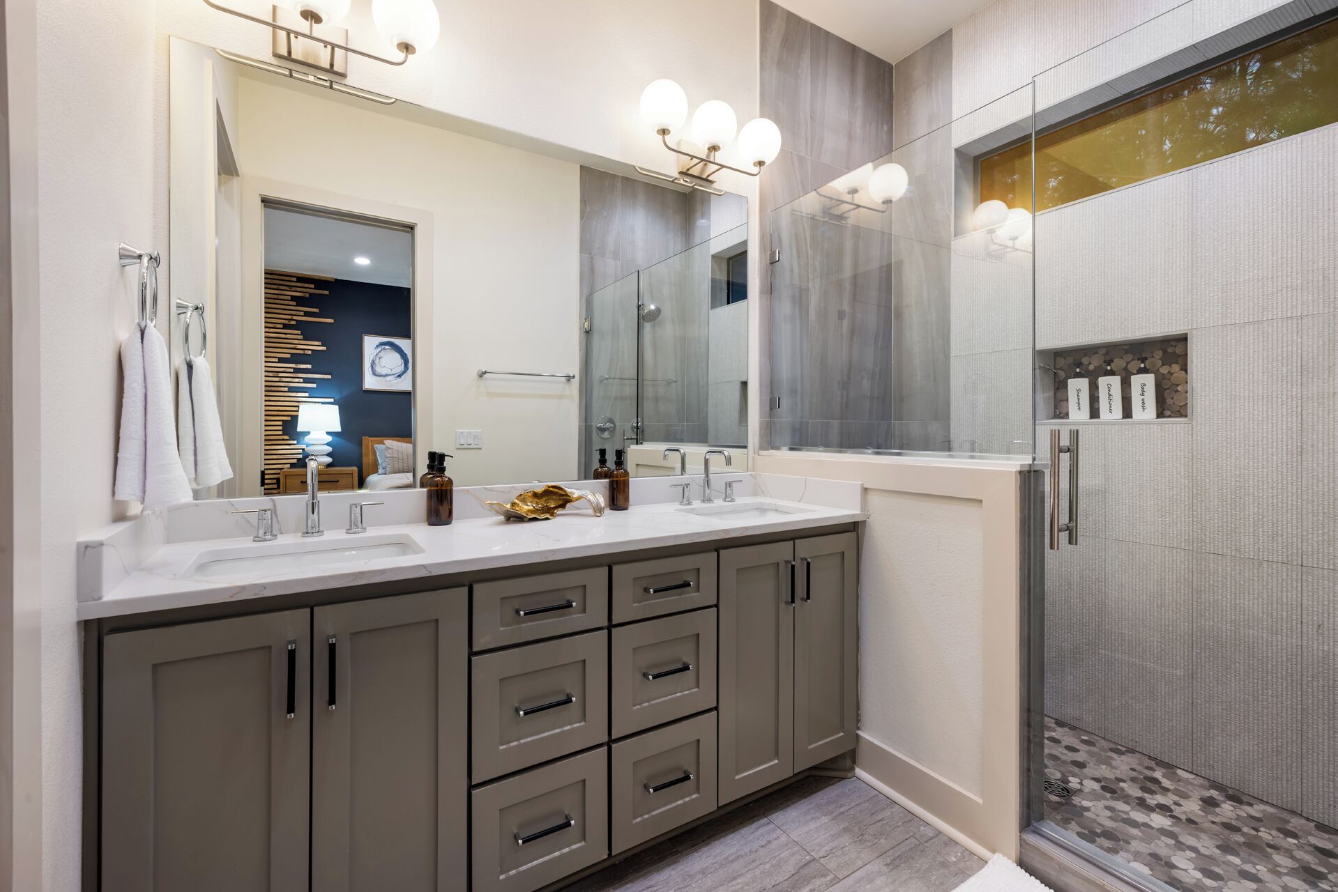 A modern bathroom with two sinks, a large mirror, and a shower area.