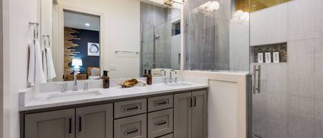 A modern bathroom with two sinks, a large mirror, and a shower area.