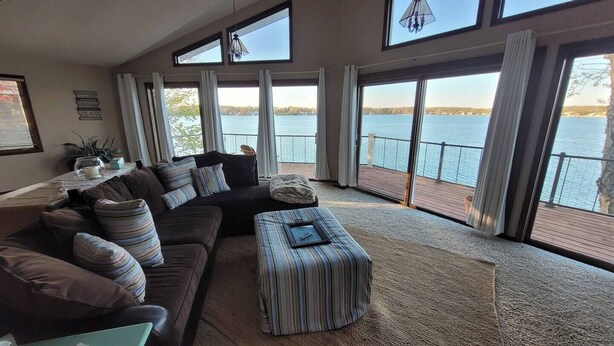 A spacious living room with a large sofa, ottoman, and a view of a lake through large windows. - Lake Gage Getaway,
Where every season feels like a vacation. (Angola)