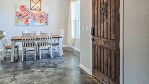 Un comedor con mesa y sillas de madera, una lámpara colgante de diseño geométrico y un cuadro abstracto de colores en la pared.