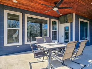 An outdoor patio with a table and chairs, large windows, and a ceiling fan.