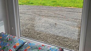 A room with a large window offering a view of a green field and gravel path.
