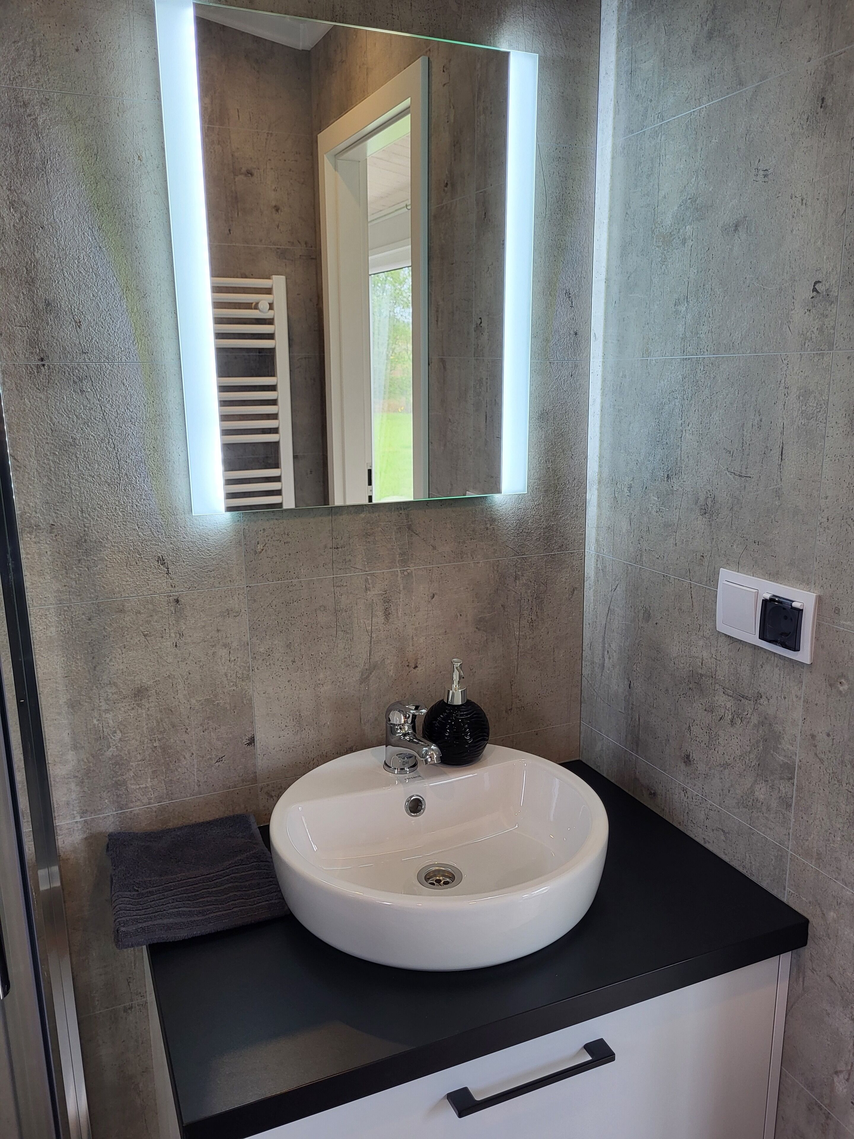 A bathroom with a white sink, a black soap dispenser, a mirror, and a towel rack.