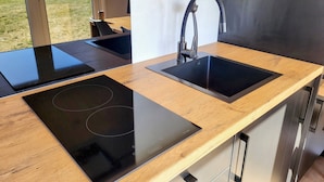 A modern kitchen with two black induction cooktops and a stainless steel sink with a sleek faucet.