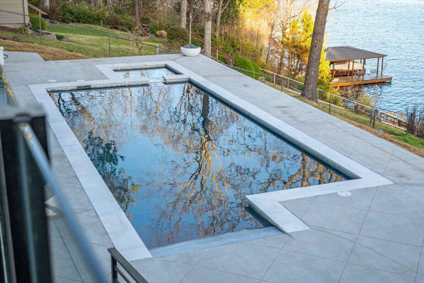 A rectangular swimming pool with a stone border, surrounded by a paved deck.