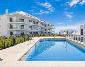 Een modern appartementencomplex met een zwembad, balkons en een helderblauwe lucht.