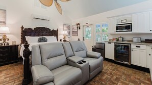 Un dormitorio con una cama grande, un sofá gris y una zona de cocina con microondas y armarios.