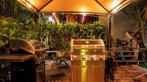 Un área de parrillada al aire libre con una parrilla de acero inoxidable, una parrilla de carbón y un toldo que proporciona sombra.