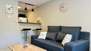 A modern living room with a grey sofa, a wooden coffee table, and two black bar stools. A clock and a wine sign are on the wall. - A- Centrally located apartment 9 de Julio I (San Carlos de Bariloche)
