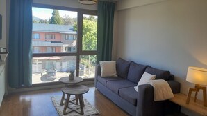 A living room with a sofa, a small round table, a lamp, and a view of buildings outside.