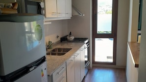 A modern kitchen with white cabinets, a stainless steel refrigerator, and a window overlooking a body of water.