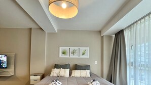 A modern bedroom with a large bed, a hanging light fixture, a flat-screen TV, and a window with curtains. - Exclusive downtown apartment (San Carlos de Bariloche)