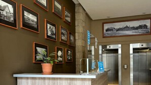 A reception desk with framed photographs on the wall, a potted plant, and an elevator in the background. - Exclusive downtown apartment (San Carlos de Bariloche)
