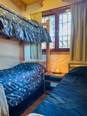 A room with two beds, a window with curtains, a nightstand with a lamp, and wooden beams on the ceiling.
