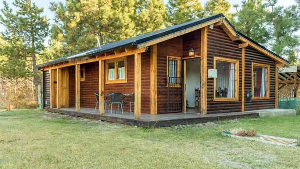 A log cabin with a porch, a dining area with chairs, and a small deck.