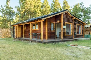 A log cabin with a porch, a dining area with chairs, and a small deck.