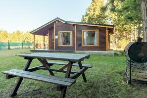 A rustic cabin with a picnic table and a barbecue grill in the yard.