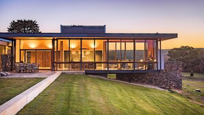Una casa moderna amb un pati espaiós, grans finestres i una paret de pedra.