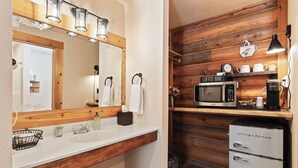 Ein Badezimmer mit einem Holzkosmetikschrank, einem Waschbecken, einem Spiegel und einer Kaffeebar mit Mikrowelle und Kaffeemaschine.