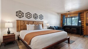 Ein Schlafzimmer mit einem hölzernen Bett, einem Schreibtisch und einem Stuhl. An der Wand über dem Bett befinden sich Kunstwerke.