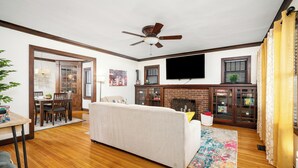 A living room with a sofa, wooden flooring, a ceiling fan, a television, and a fireplace.