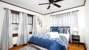 A bedroom with a bed, curtains, a ceiling fan, and a nightstand with a lamp.
