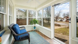 A sunroom with a ceiling fan, a wicker chair with blue cushions, a potted plant, and a view of the backyard.