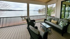 A covered deck with a view of a lake, wicker furniture, and a ceiling fan.