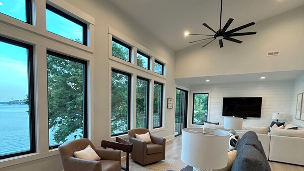 A spacious living room with large windows, a ceiling fan, and a flat-screen TV.