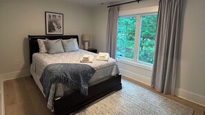Een slaapkamer met een bed, een raam met gordijnen, een nachtkastje en een wandlamp.