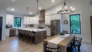 A modern kitchen with white cabinets, a central island, and a dining area with a long table and chairs.