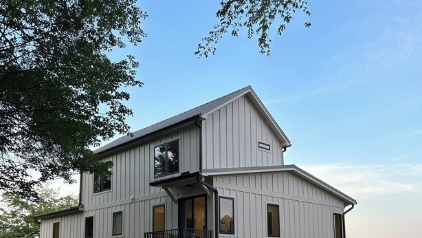 Een tweelaags huis aan het water met een balkon, buitenmeubilair en een steiger die in het water uitloopt.