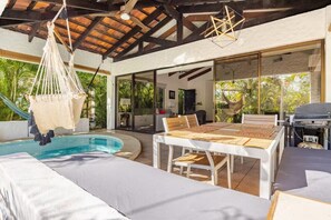 Un área junto a la piscina con mesa y sillas, una hamaca colgante y una parrilla.